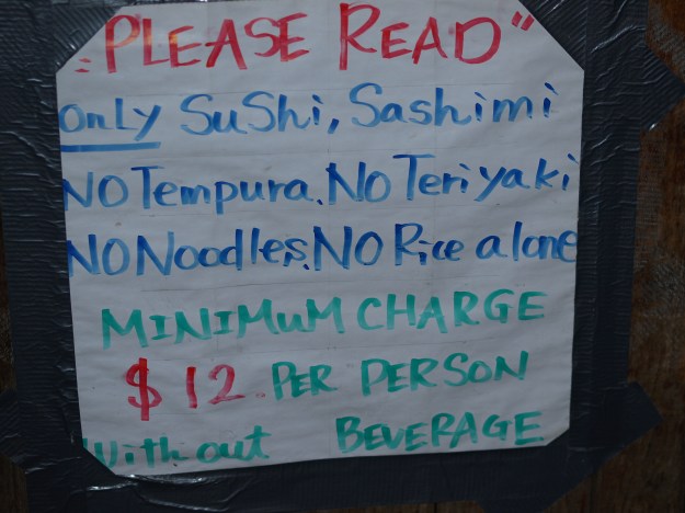 Photo of hand-lettered sign that reads "please read. only sushi, sashimi. no tempura. no teriyaki. no noodles. no rice alone. minimum charge $12 per sperson without beverage."