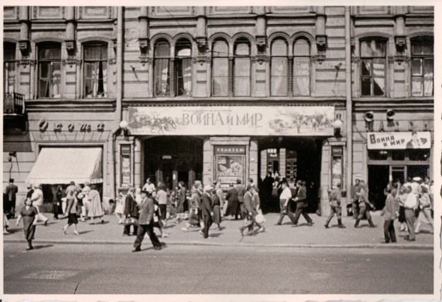 {Black and white photograph of people walking in front of a building with a large banner in Russian.}