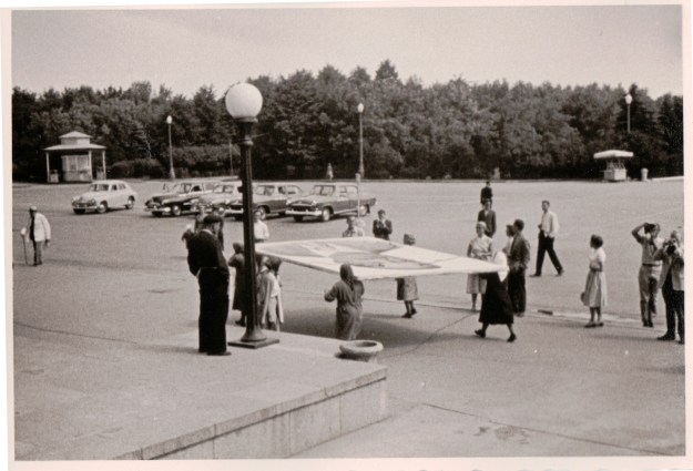 {Black and white photo of a giant portrait being carried horizontally by five women in scarves.}