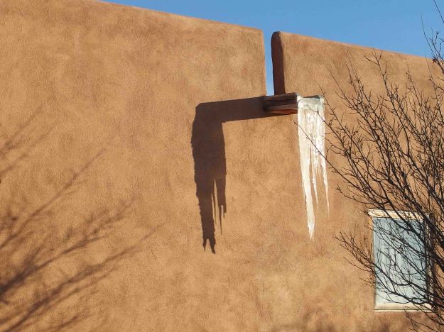 {Image:  a flat water spout protrudes from an adobe wall with several feet of frozen water suspended off the end.}