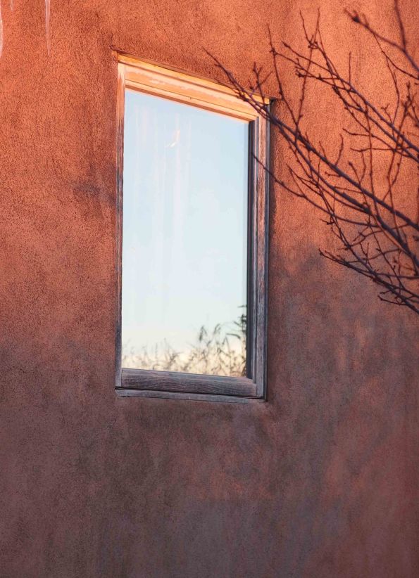{Image:  a window in an adobe wall.  The window reflects a very blue sky.  Tree branches enter the photo from the right.}