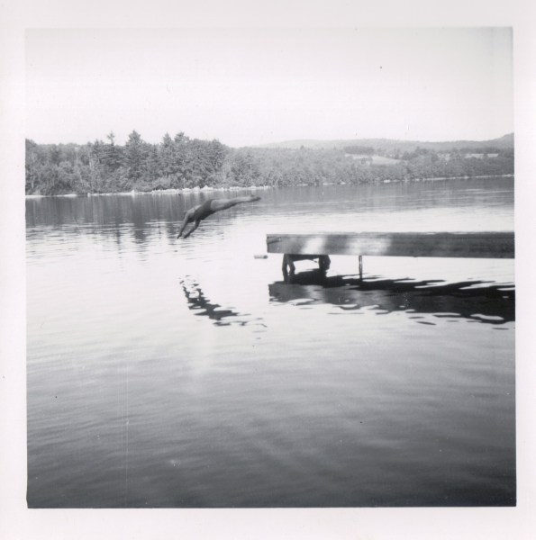 {Image: black and white photo of a person diving off of a dock into a lake.  The diver's image is reflected in the lake.}