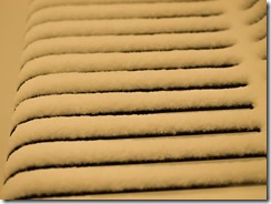 {Image:  close up of the slats on a metal bench covered with about a half-inch of snow.}