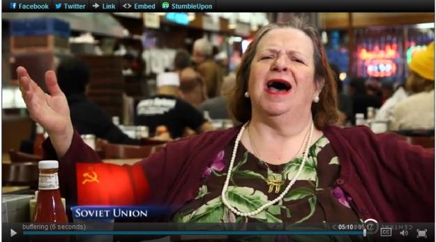 {Image: White woman with dark hair and flowered dress with a necklace bearing the Hebrew letter "chai". Her arms are outstretched to the side and her mouth open in song. image of the soviet flag (yellow hammer & sickle against a red background) and the words "Soviet Union" in the lower lefthand corner.}