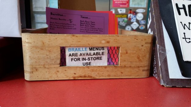 Photo:  wooden box containing menus; a sign on the side reads "Braille menus are available for in-store use." 