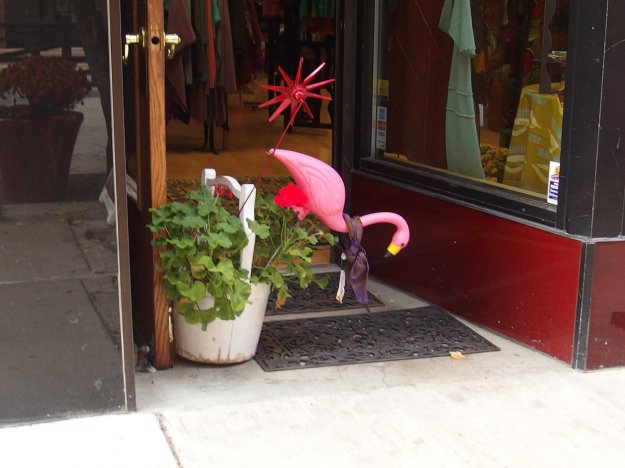 Photo of store with level entry, which put a flower pot in the door, and in the flower pot, a large plastic pink flamingo which is pitching face first into the door width. 