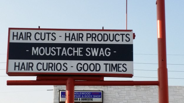 Image: large commercial sign reading "hair cuts.  hair products.  moustache swag. hair curios. good times." 
