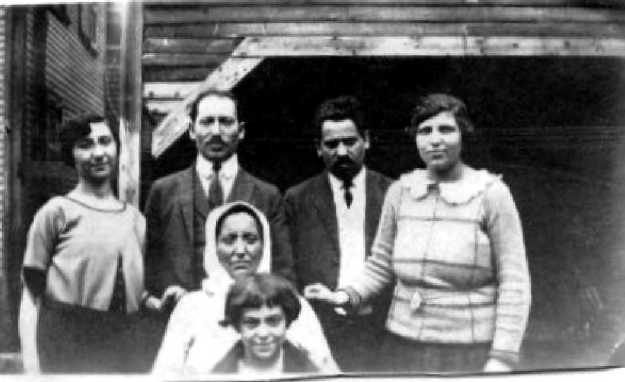 Image:  slighly blurry black & white photo of a group of 6 people.  In back, a young woman, two middle aged men and a middle aged woman; in front of them, an older woman, and in front of her, a child of about 10.