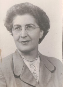 Image:  black & white photo of a middle-aged woman with short salt & pepper hair and wire-rimmed glasses, wearing a suit jacket and a lace blouse underneath