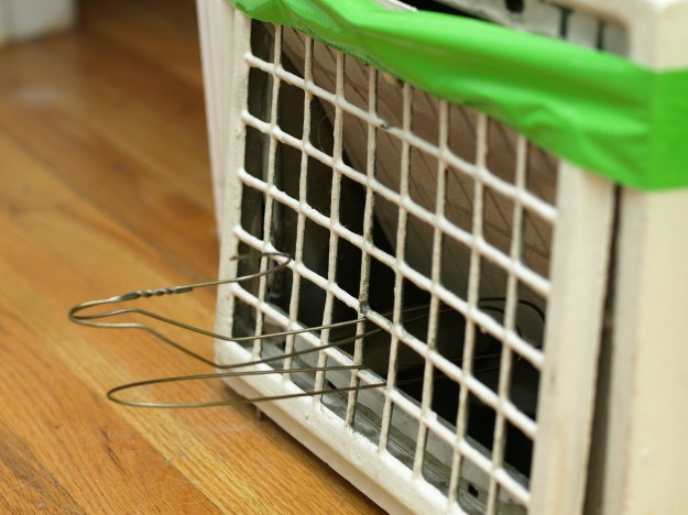 Image: an old metal heating grate, taped to the wall with green duct tape, held open with a wire coat hanger.