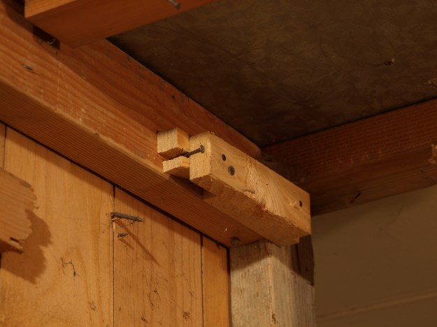 Image:  several layers of pieces of wood nailed together - and splitting -- on the side of a wall.  