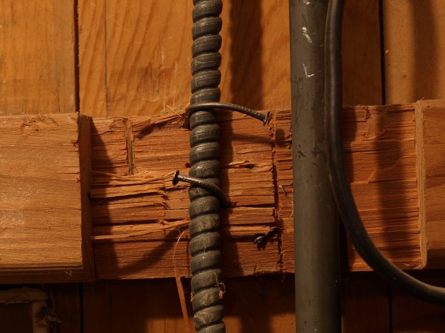 Image: close up of electrical casing attached by bent nails to hacked up 2x4