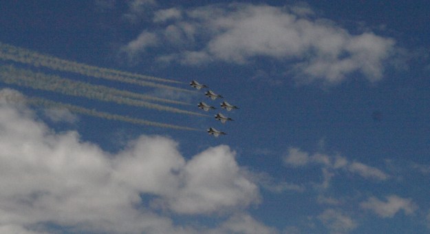 Image: six fighter jets flying in tight formation with contrails.