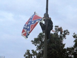 Image: African American woman in climbing gear and helmet, climbing down a flag pole with the Confederate flag in her hands.