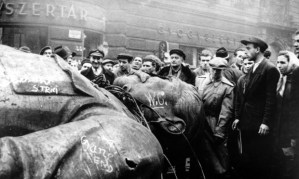 Image: Black and white photo of men gathered around the head and chest of an enormous statue of Lenin lying prone on the ground.
