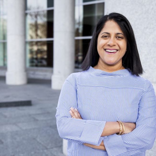 Image: photo of woman with brown skin and shoulder length brown hair in a striped shirt, facing the camera smiling.