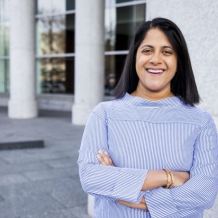 Image: photo of woman with brown skin and shoulder length brown hair in a striped shirt, facing the camera smiling.