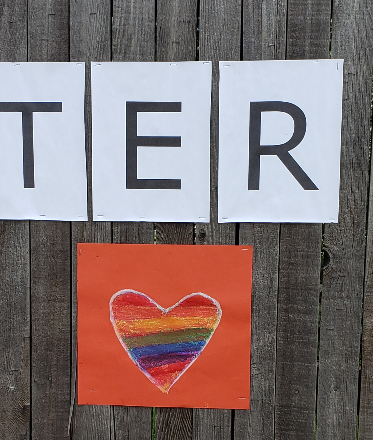 Orange construction paper sign with a heart outlined in white and filled in with rainbow colors.