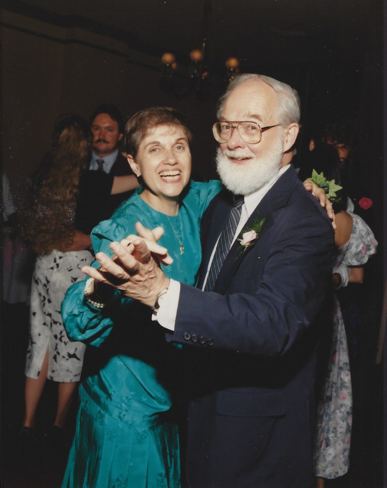 Ruth (white woman with brown hair and a blue-green dress) and David (white man with white hair and beard, wearing a suit and tie). They are dancing with beautiful smiles on both faces.