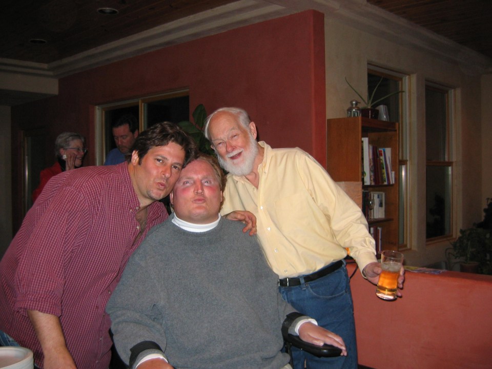 Three men at a party. Jeff (white man; red shirt); Tim (white man; gray fleece; wheelchair); David (white man; white hair/beard; yellow shirt).