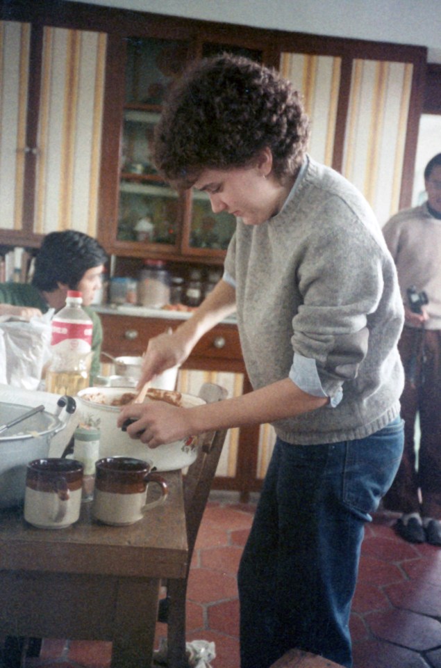 Amy in gray sweater stirring something in a kitchen .